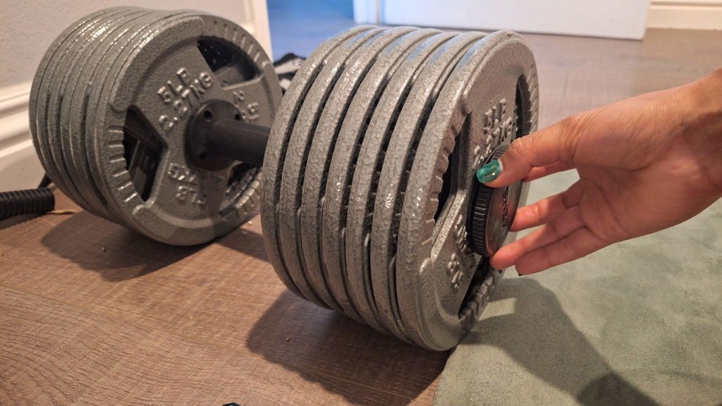 A hand spinning the AdaptaBELL collar down against a stack of old grey cast-iron Olympic plates on a wooden floor.