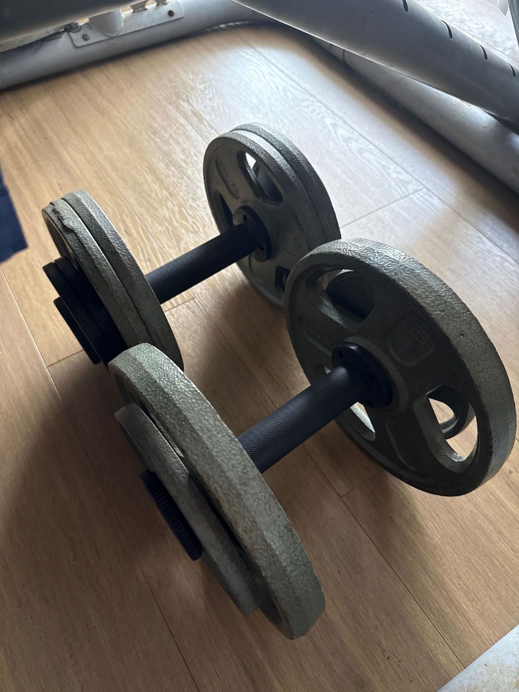 A pair of loaded AdaptaBELL dumbbells resting on a wooden floor, made up with mismatched grey Olympic plates of different ages.
