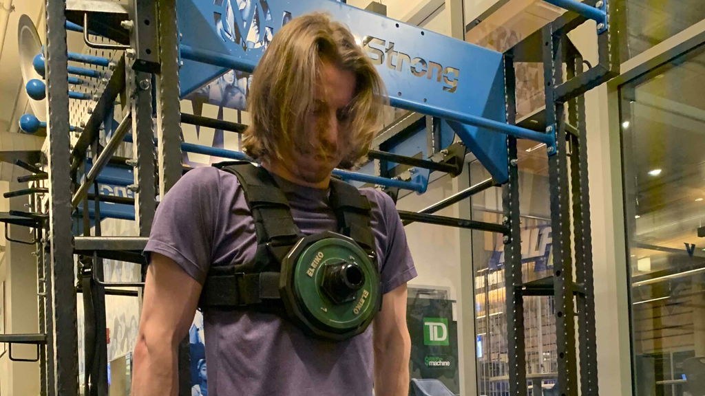 A man doing a dip at a squat rack wearing a Kensui EZ-VEST loaded with a single green weight plate on the chest