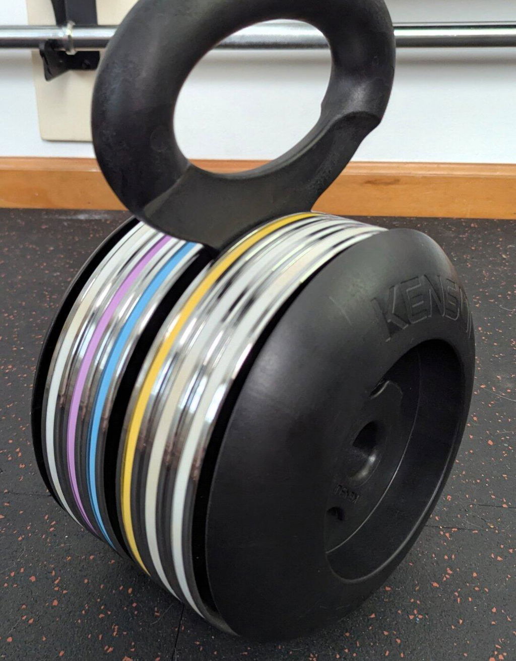 A Kensui EZ-BELL loaded with a stack of calibrated steel plates standing on a rubber gym floor
