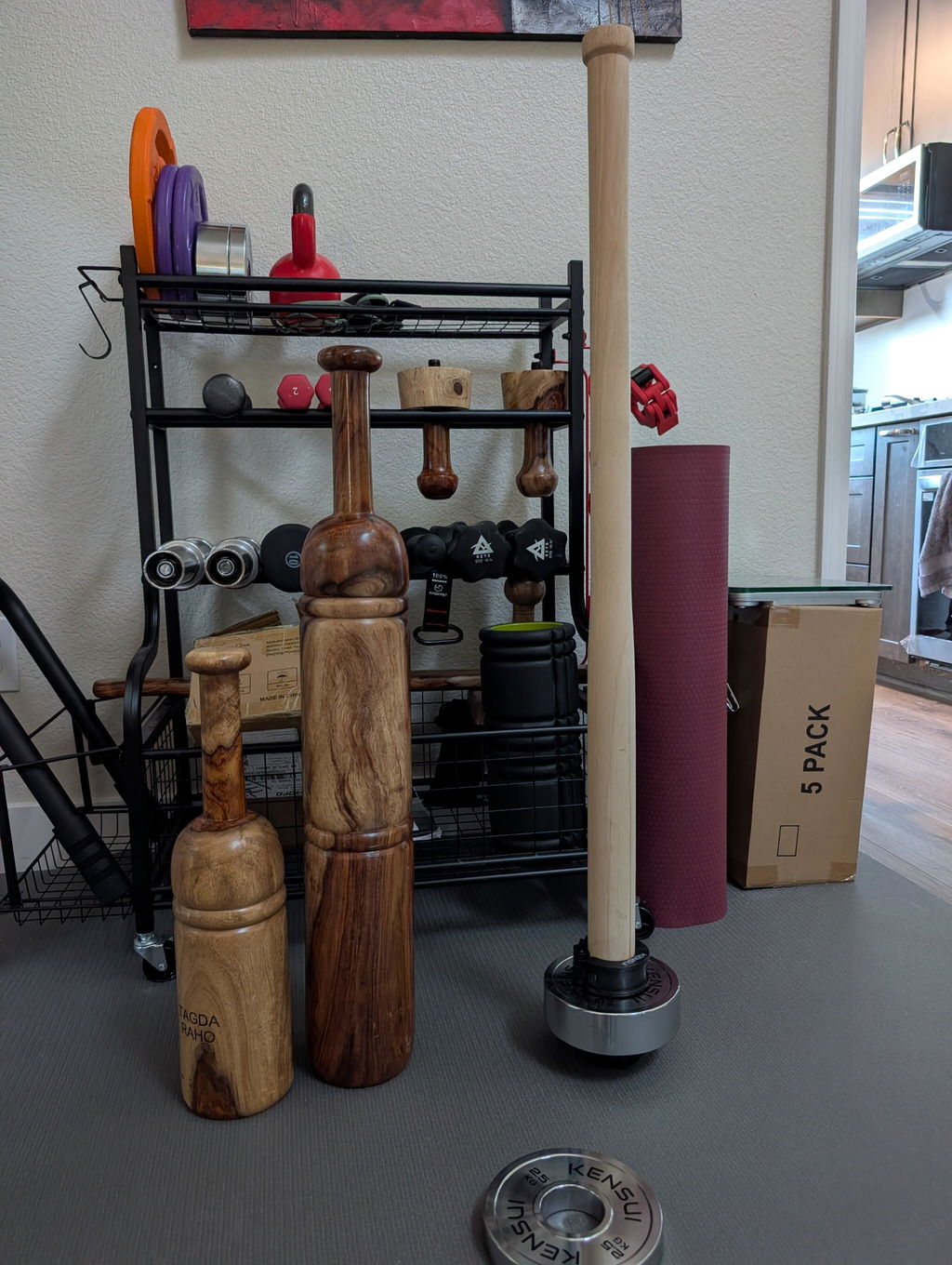 EZ-Mace V2 standing next to two traditional Indian wooden gadas in a home gym