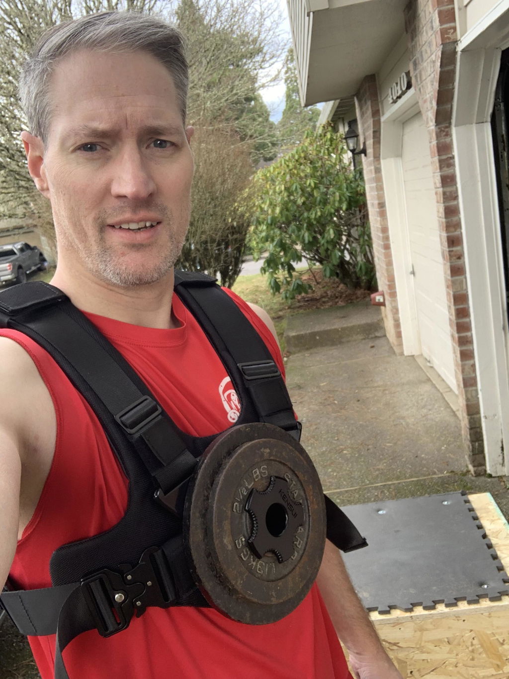 Man in a red tank top wearing a plate-loaded vest on a driveway