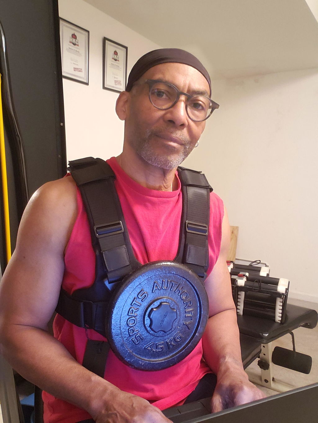 Lifter in a pink tank top wearing the vest loaded with a blue plate