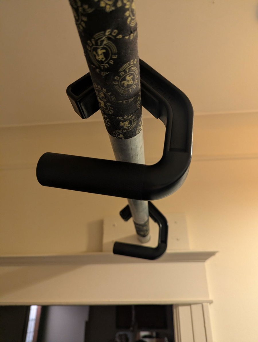 Black neutral grip handle hooked over a tape-wrapped pull-up bar mounted above a doorway