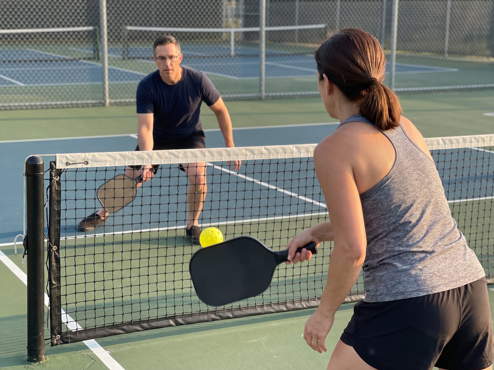 The author's wife, seen from behind at the kitchen line, sending a low ball over the net as the author crouches to reach it
