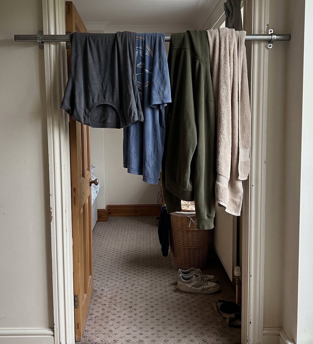 A pull-up bar across a hallway doorway with shirts, a jacket and a towel hung over it